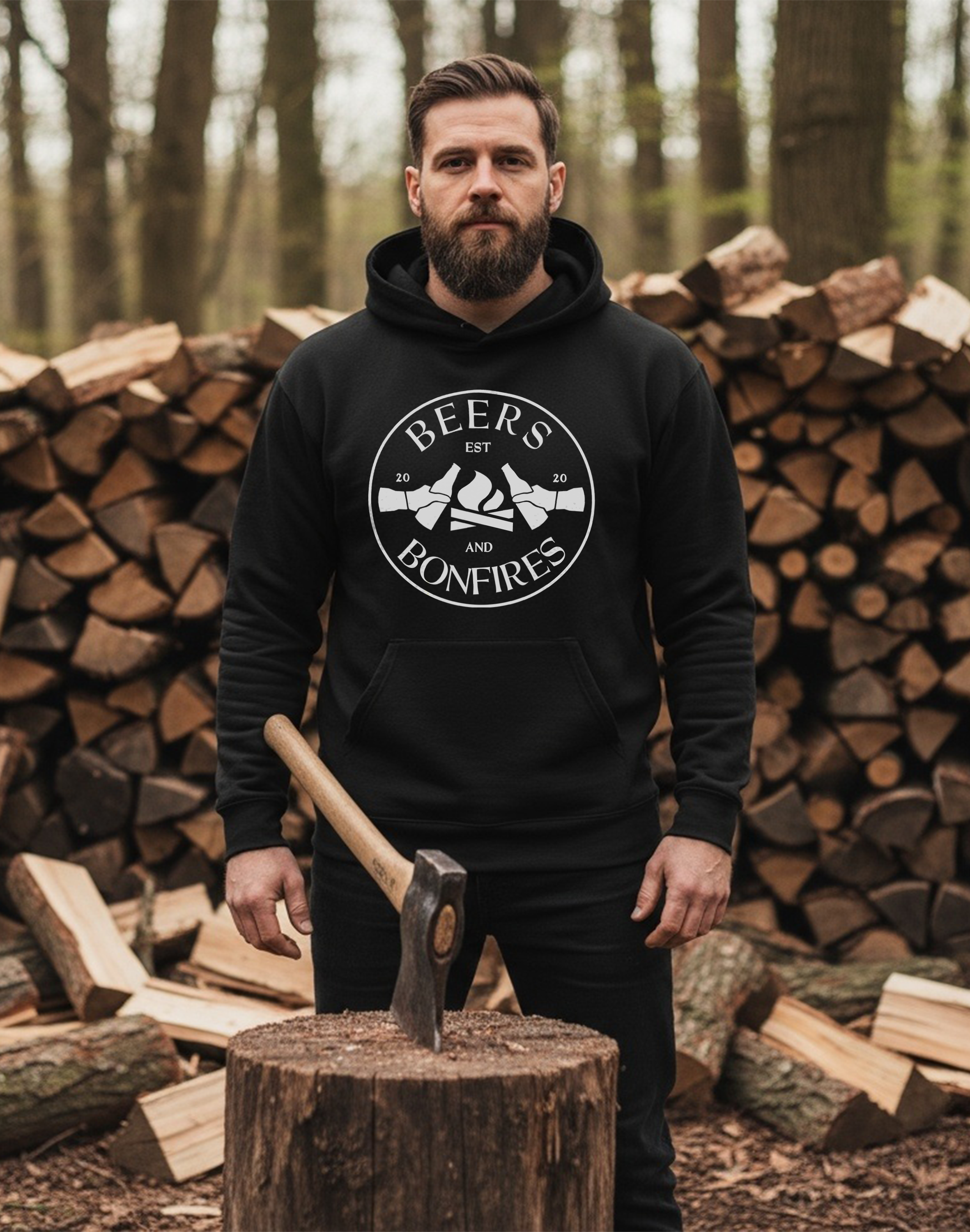 Man wearing a black hoodie with 'Beers and Bonfires' logo, holding an axe in front of stacked logs.