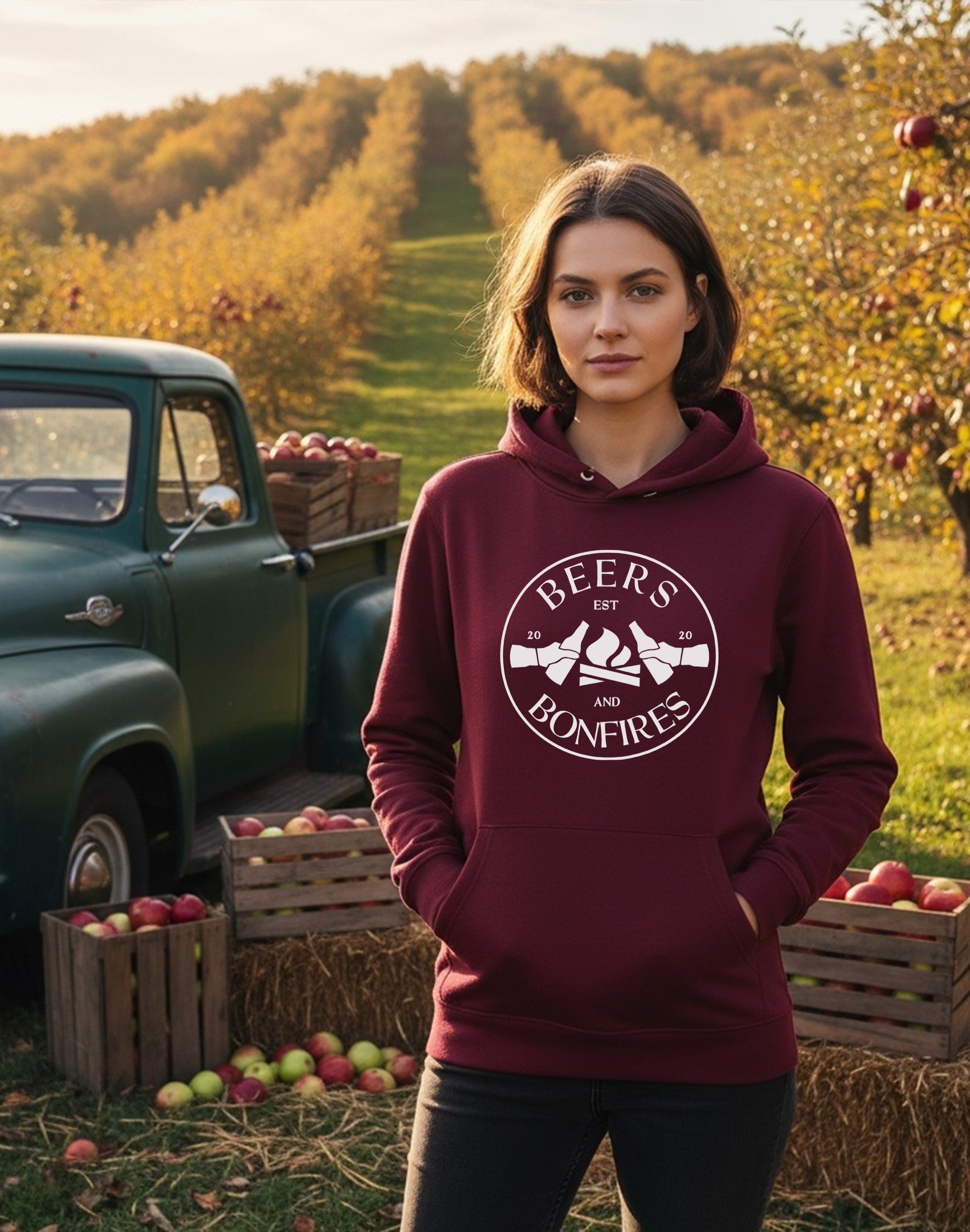 Lady wearing a maroon hoodie with Beers and Bonfires design in an apple orchard.